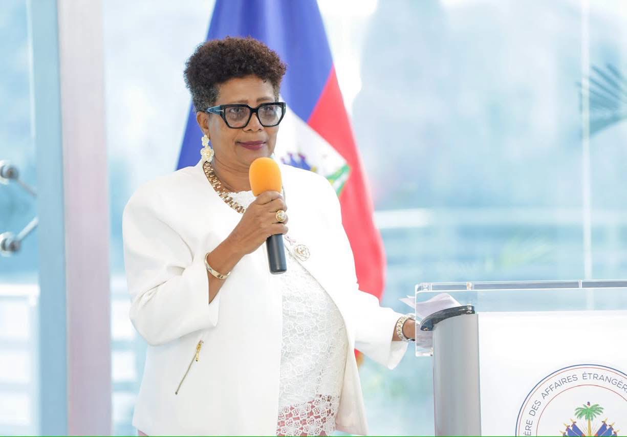 Participante vêtue de blanc intervenant au microphone devant le drapeau haïtien lors d’une activité Octobre Rose