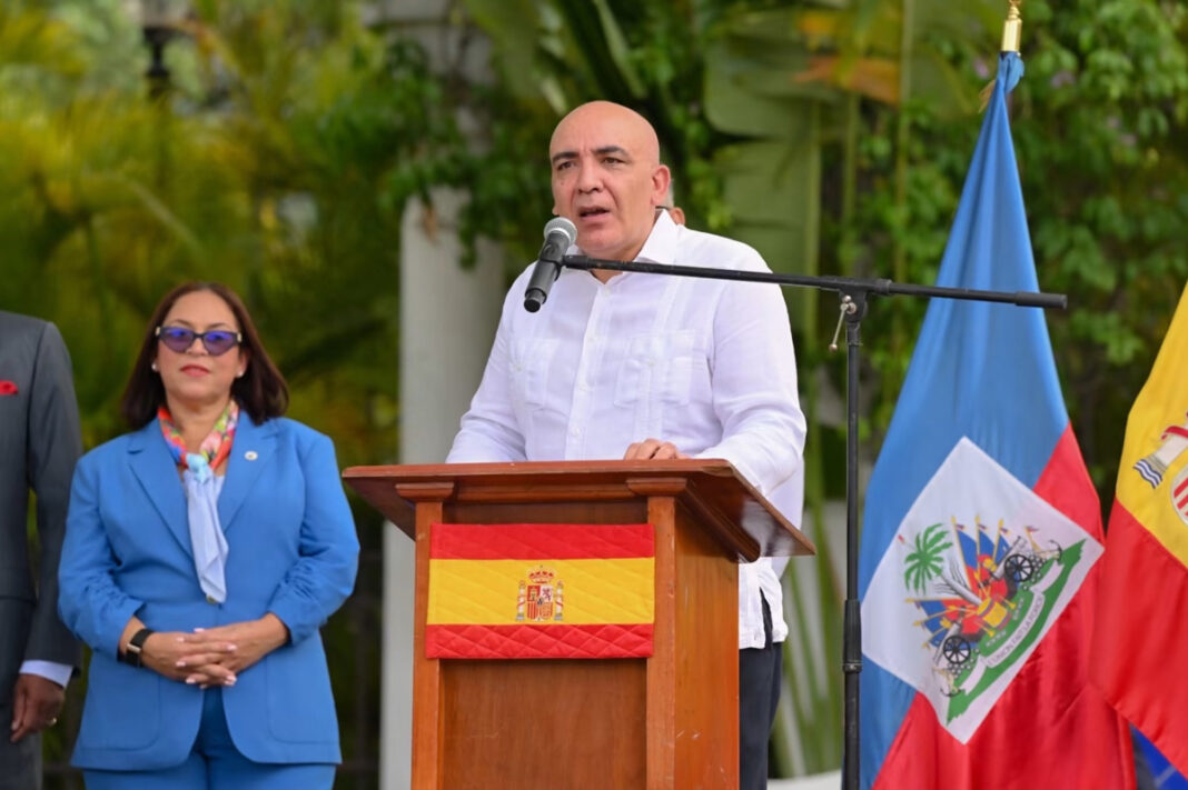 L’ambassadeur d’Espagne en Haïti prononce un discours devant les drapeaux espagnol et haïtien lors d’une cérémonie officielle.